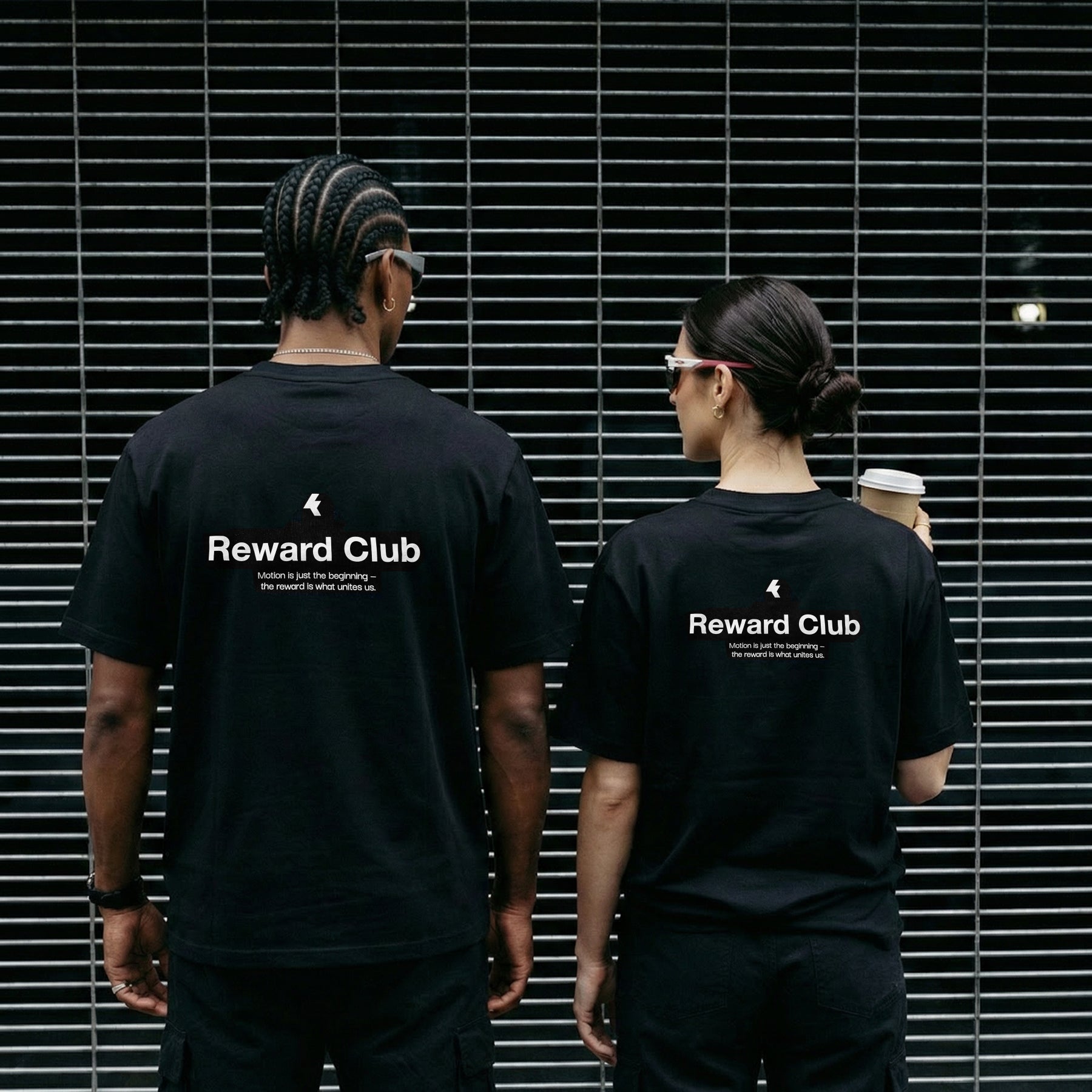 Two people wearing black kamo t-shirts in front of a metallic background