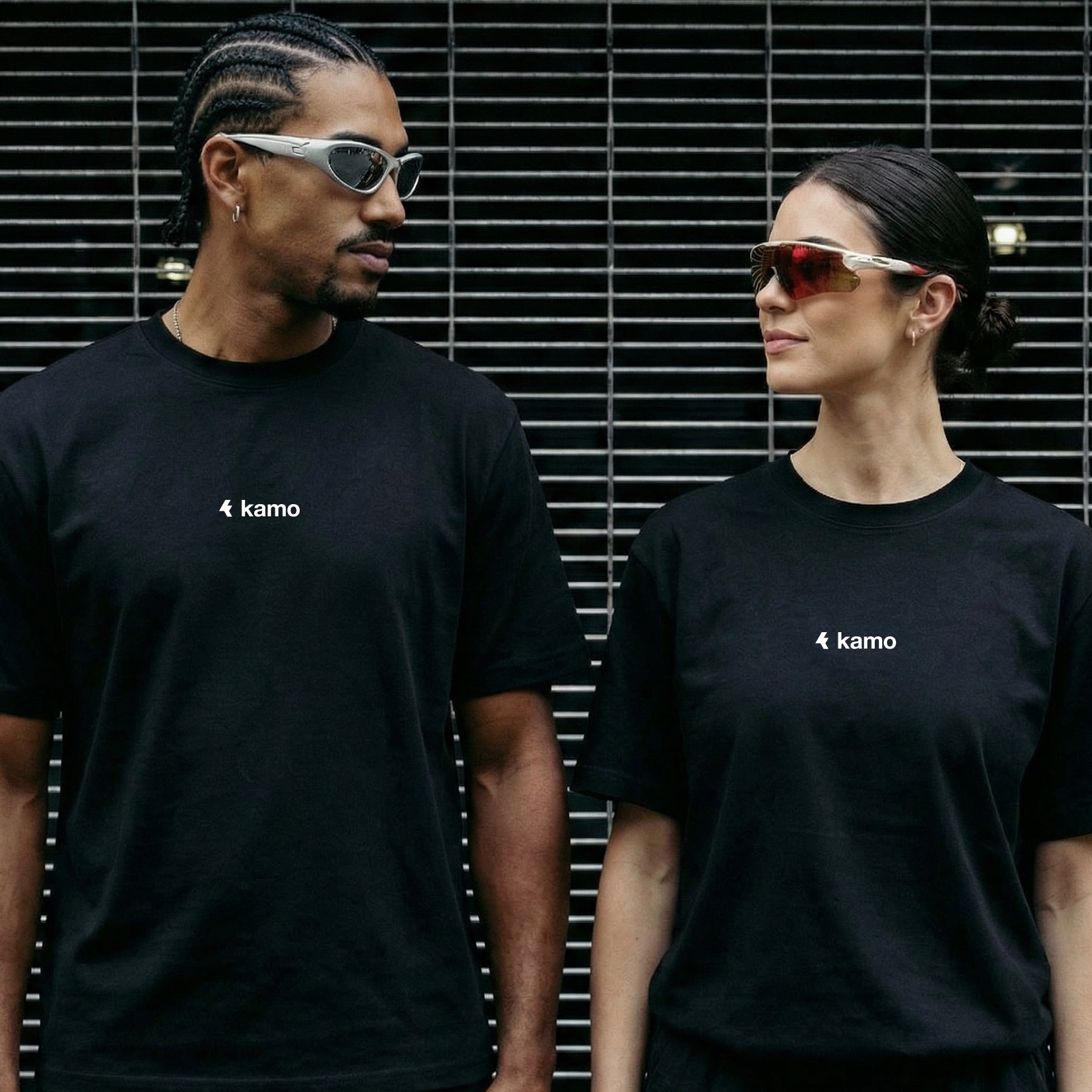 Two people wearing black kamo t-shirts in front of a metallic background